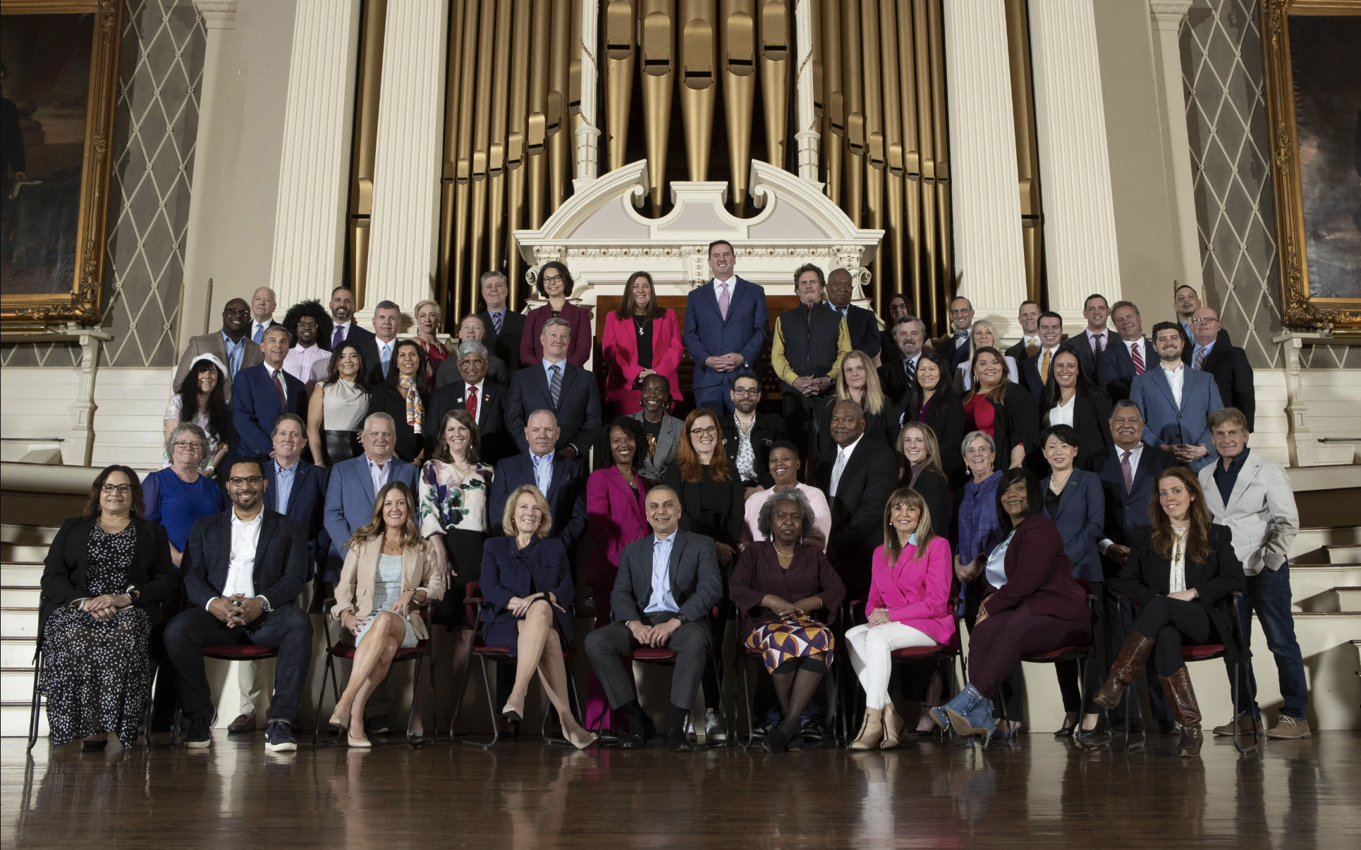 A group of 100 people standing on a stage at Worcester's Mechanics hall. They are in professional dress and are facing the camera, smiling.